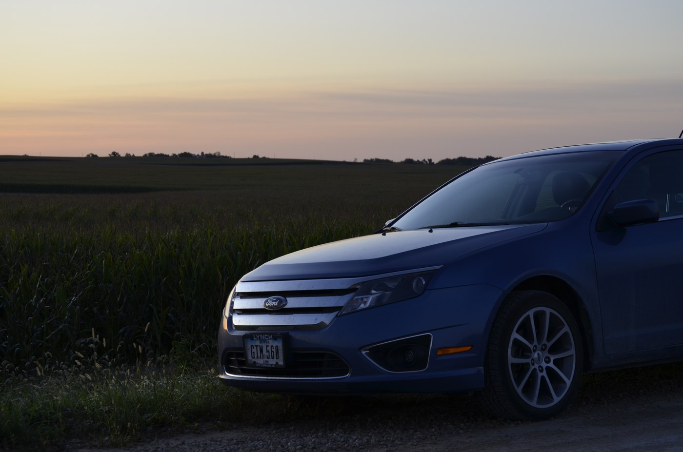 A car parked along the edge of an Iowa cornfield at dusk