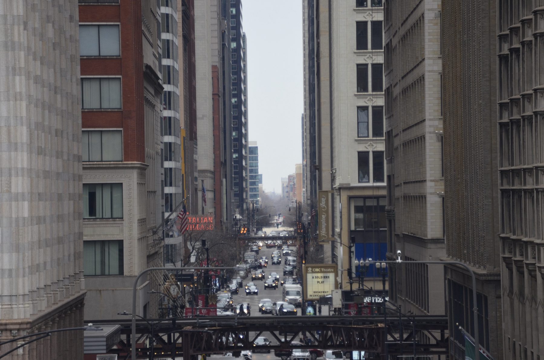 A busy Loop street seen from above, crossed by elevated L tracks and lined with tall stone buildings