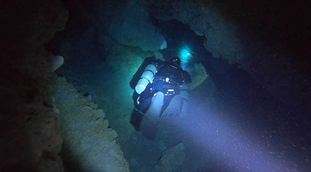 Diver in a submerged cave passage, lit by a distant blue light